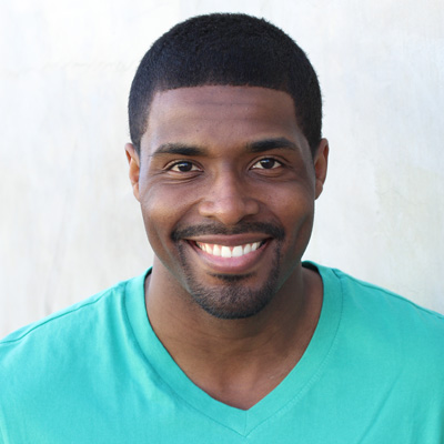 An elderly couple sitting closely together, smiling and looking directly at the camera.